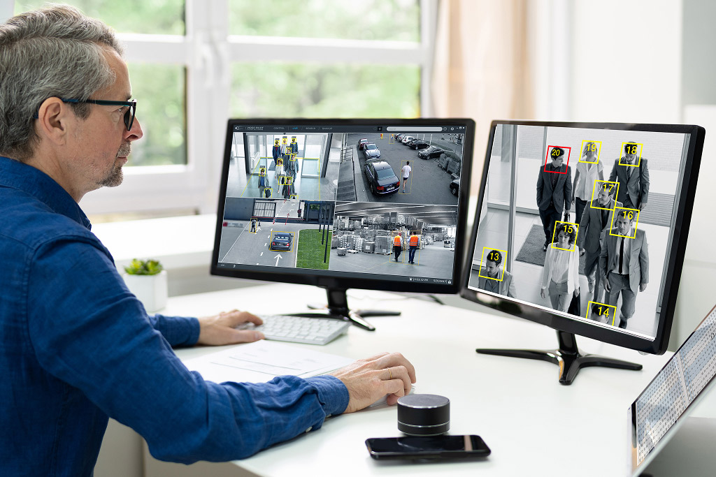 Person monitoring retail security footage on two screens showing store areas and clothing detection